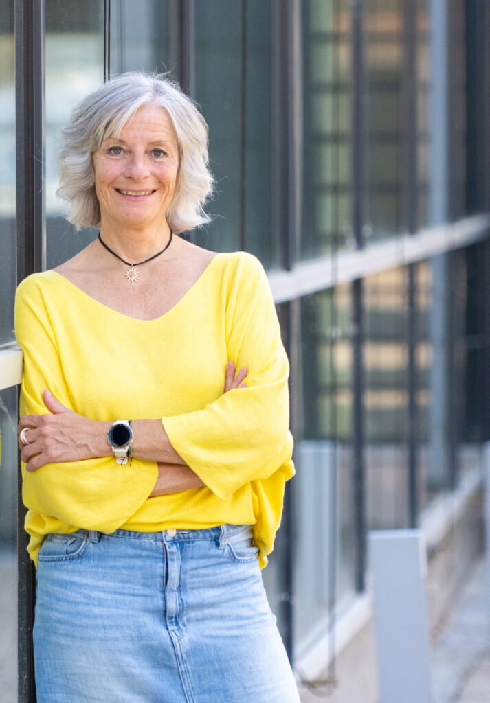 Sandra Jost, angelehnt an Glasfront, gelbes Shirt